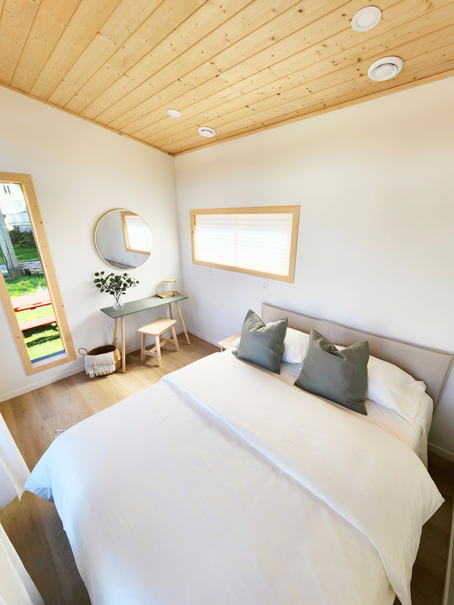 a small cabin bedroom with a white bed and pine wood ceiling
