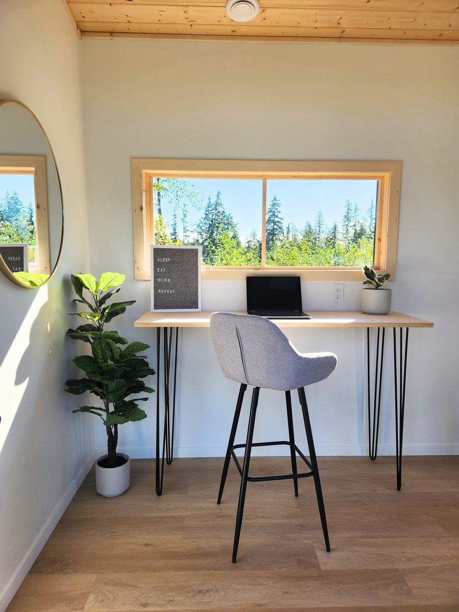 a backyard office with a desk, chair and potted plant and window looking out onto a forest